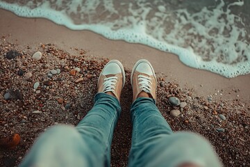 Naklejka premium Top View of Feet in Sneakers Standing on Sandy Beach Near Ocean Waves