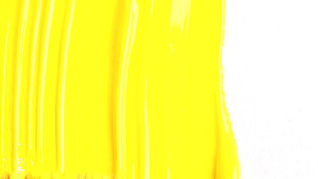 Painting yellow vertical strokes on white canvas, macro shot. Close up of artists hand holding paint brush and drawing gouache or oil painting.