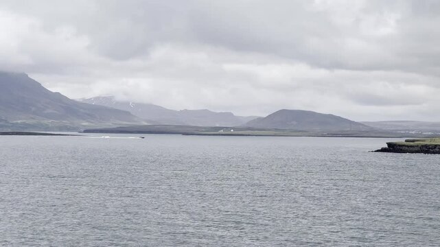 Reykjavik, Iceland - small boat entering the port by Reykjav&iacute;kurborg coastline and cloud covered mountain Esjan on scenic cruise