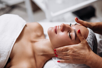 Cosmetologist doing a face and neck massage in beauty salon. Self care spa concept. Portrait of an attractive, relaxing woman. Advertising of cosmetology and cleanliness.