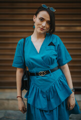 Young woman in blue dress standing outdoors with confident expression, stylish accessories, and...