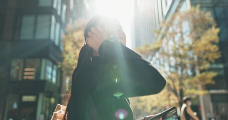 Asian, business woman and earpods in city, walki for travel and lens flare, commute to work and music. Cityscape, smartphone and listening to radio on journey, professional in Tokyo and urban street - Powered by Adobe