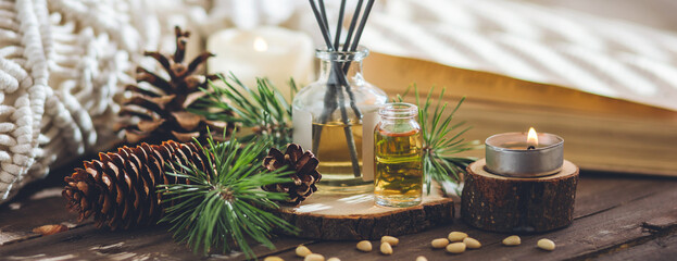 Aromatic home apartment diffuser with the fresh pine fragrance. Spruce, fir tree branches, wooden background. Essential oils, candle as table decor. Cozy atmosphere, Christmas spirit. Banner