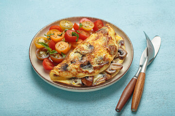 Delicious omelette with roasted mushrooms served with fresh cherry tomatoes and basil on blue background for healthy breakfast or lunch from above