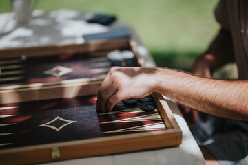 Close-up of a hand strategizing in backgammon outdoors. Sunlight creates a relaxed atmosphere perfect for leisure and focus.