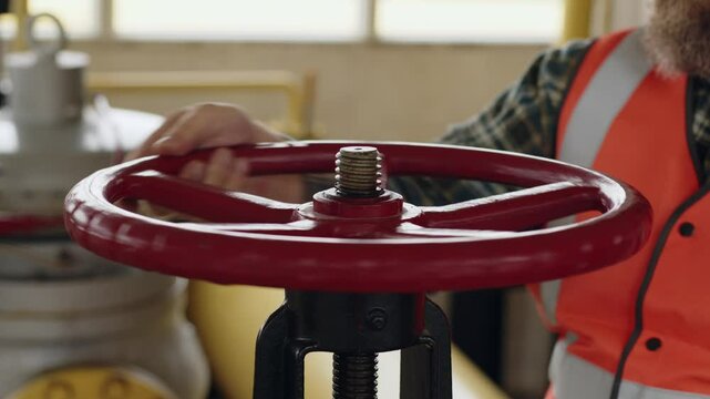 Worker adjusting red industrial valve with hand wearing safety vest in workplace