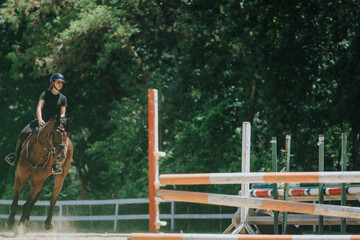 A young equestrian skillfully rides a horse during an outdoor show jumping competition, showcasing...