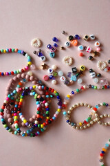 Colorful DIY necklaces, friendship bracelets and various plastic beads on pastel pink background. Flat lay.