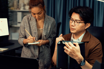 Managers discussing on document paperwork together for business planning on market share data at over late night time at modern home office, working on startup company deadline project job. Infobahn.