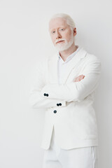 Portrait of a stylish elderly man with white hair and beard, wearing a white suit against a plain...