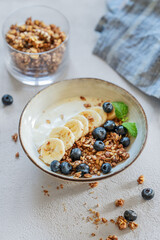 Greek yogurt with granola or muesli, banana and blueberries in a bowl on a white background