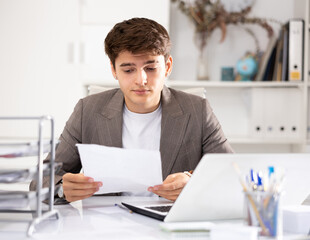 Obraz premium Male bookkeeper doing paperwork in his workplace in office - checks accounting documents