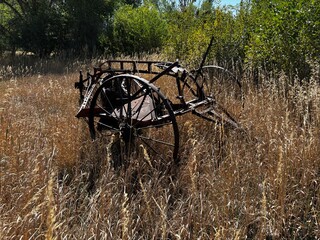 Old rusted metal farm plowing equipment in field with metal wheels