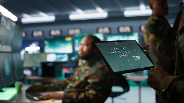 Military agent working in control room, using software on tablet, analyzing aerial reconnaissance data. Close up of intelligence corps expert controlling drones with portable device, camera B