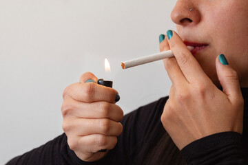 Obraz premium Close up to a young woman trying to light on a cigarette with a lighter with blurred background