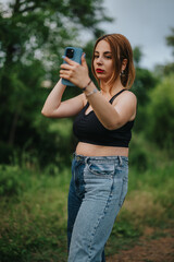 A young woman captures a selfie in a lush green park, showcasing casual fashion and modern technology use.