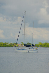 Vertical view out over calm blue water towards blue and white sailboat at Big Bayou water towards...
