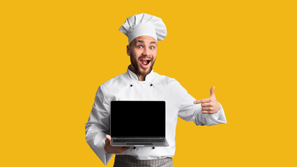 Excited Chef Cook Man Showing Laptop Empty Screen And Gesturing Thumbs-Up Approving Culinary Website Standing On Black Studio Background.
