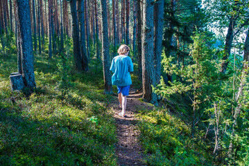 Obraz premium 11 year old boy in shorts, t-shirt and flip flops walking along path in pine forest, back view