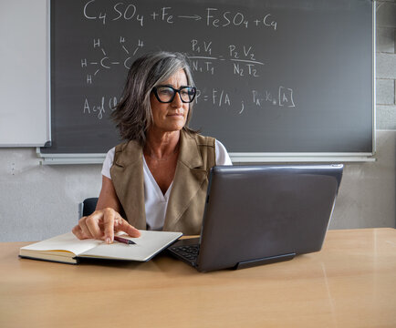Middle-aged female teacher working with a notebook and a laptop in a high school or university. Science teacher