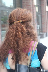 A woman walks down a city street showcasing her curly hair adorned with a decorative hair clip...