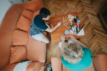 A young boy enjoys a game of pick-up sticks with his grandmother in a cozy living room setting. The...