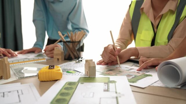 Smart architect and safety engineer discussion about building blueprint on table with architectural document, measurement tools and wooden block scatter around at modern office. Closeup. Delineation.