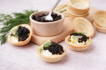 Tasty tartlets with black caviar on light background