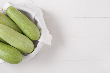 Bowl with fresh green zucchini on white wooden background