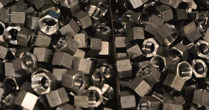 Slow motion of the hardware nuts in the box. Close-up of large pile of hardware nuts. Metal surfaces shining in the light. Mixed up hexagonal pieces.