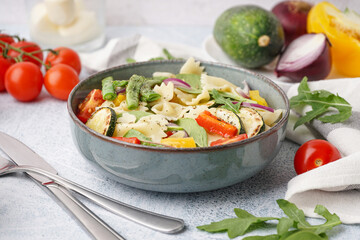 Bowl of tasty pasta salad with pepper and tomatoes on white background