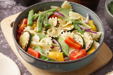 Bowl of tasty pasta salad with pepper and red onion on dark background