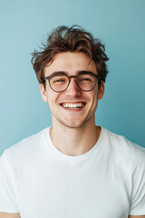 Fototapeta premium Young Caucasian man with glasses, smiling confidently, projecting energy and enthusiasm, set against a light blue background.