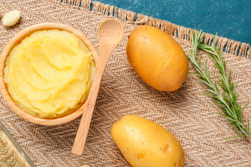 Wooden bowl of tasty mashed potatoes with garlic and rosemary on blue background