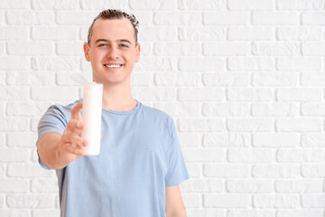 Young man with bottle of shampoo on white brick background