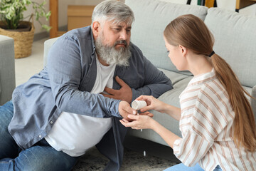 Young woman giving medicine to her father who is having heart attack at home