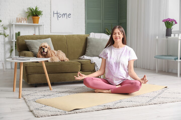 Sporty young pregnant woman with cocker spaniel meditating at home