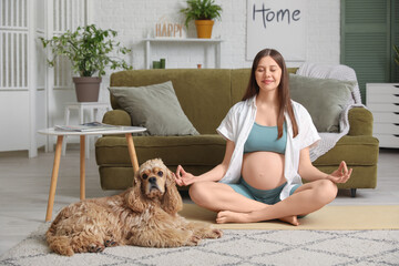 Sporty young pregnant woman with cocker spaniel meditating at home