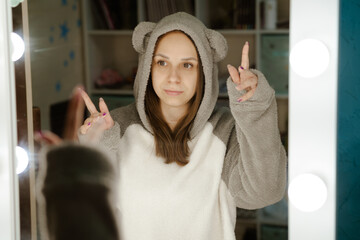 A young woman dances energetically in front of a mirror in her bedroom. Shes wearing a grey hoodie and smiling as she moves.