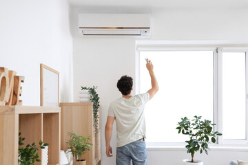 Young man switching  on air conditioner at home