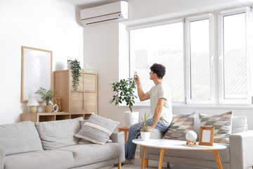 Young man switching  on air conditioner at home