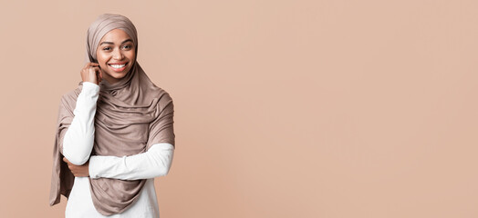 Portrait of shy afro muslim girl in hijab sincerely smiling, posing over yellow background with empty space © Prostock-studio