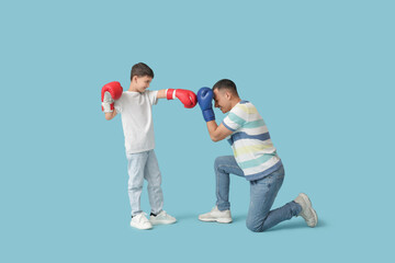 Cute little boy with his father in boxing gloves on blue background