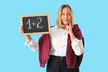 Mature female math teacher with small blackboard on blue background