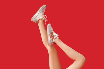 Legs of young woman in stylish sneakers on red background