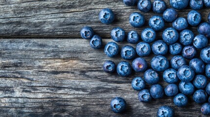 A close-up of fresh blueberries scattered across a rustic wooden table, with a few placed in a neat pile.