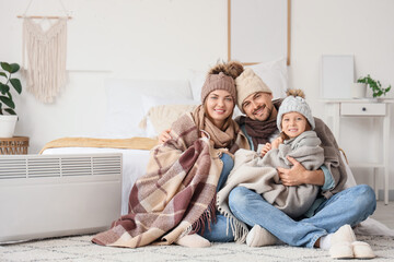 Little girl and her parents with warm plaids hugging near radiator in bedroom