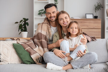 Little girl and her parents with warm plaid sitting on sofa at home