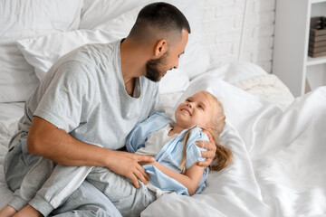 Father tickling his little daughter in bedroom