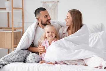 Fototapeta premium Happy parents and their little daughter with soft blanket sitting in bedroom